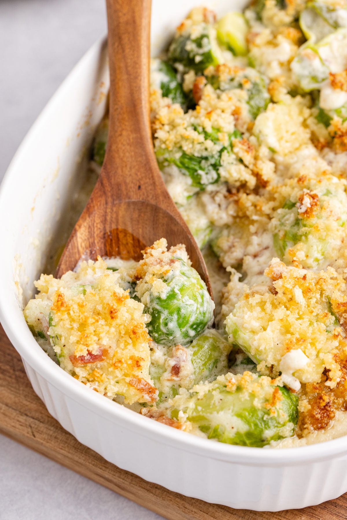 A wooden spoon scooping up a casserole with Brussels sprouts.