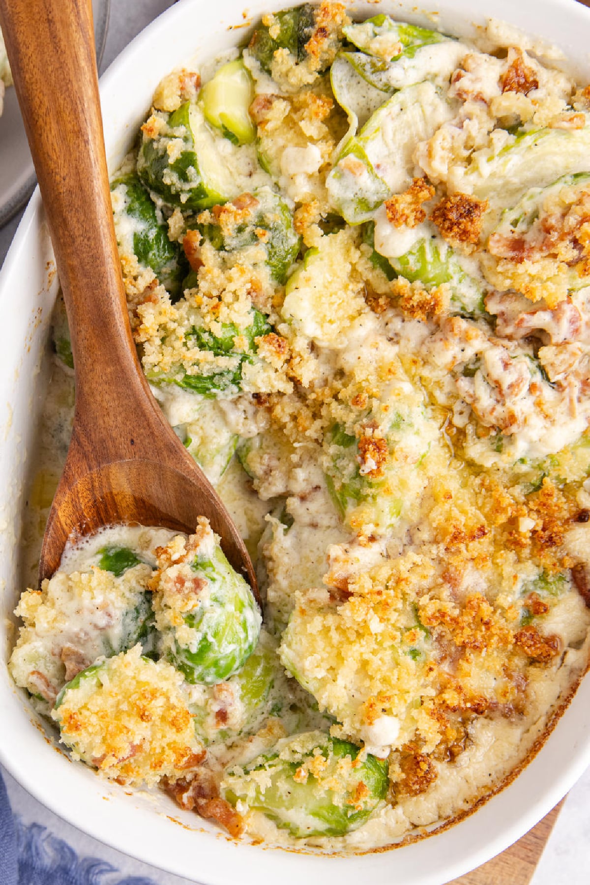 A casserole dish filled with Brussels sprouts, sauce and cheese being scooped up.
