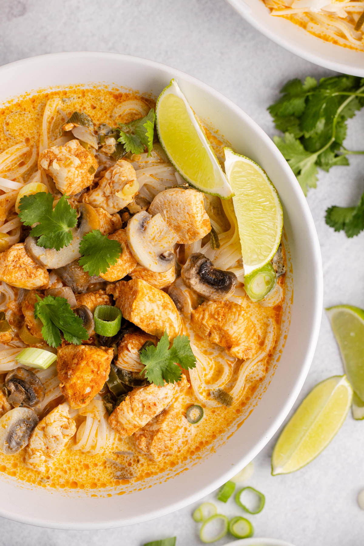 A bowl full of soup with chicken, mushrooms, scallions and served with lime on the side.