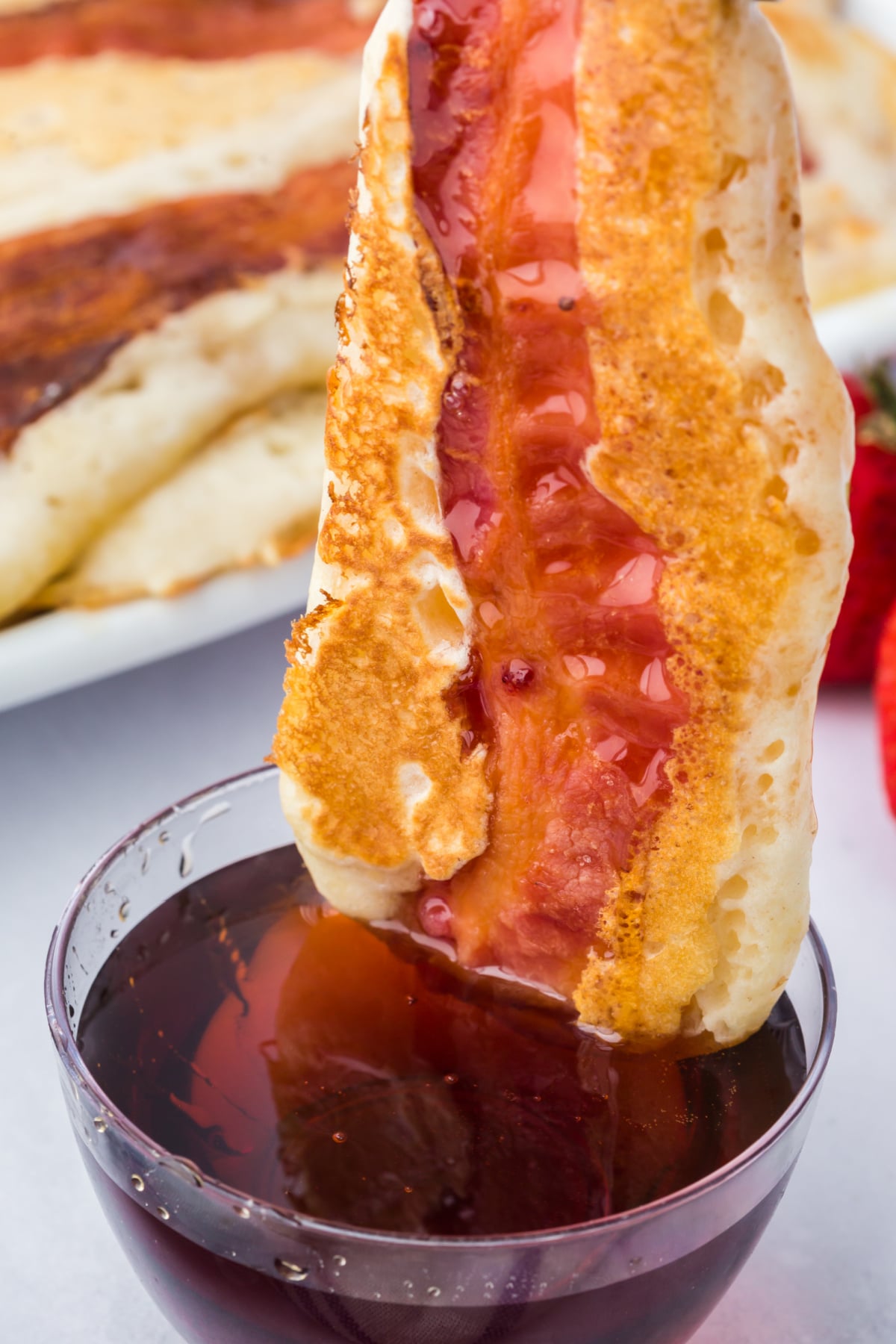 A pancake dipper being dipped into syrup.