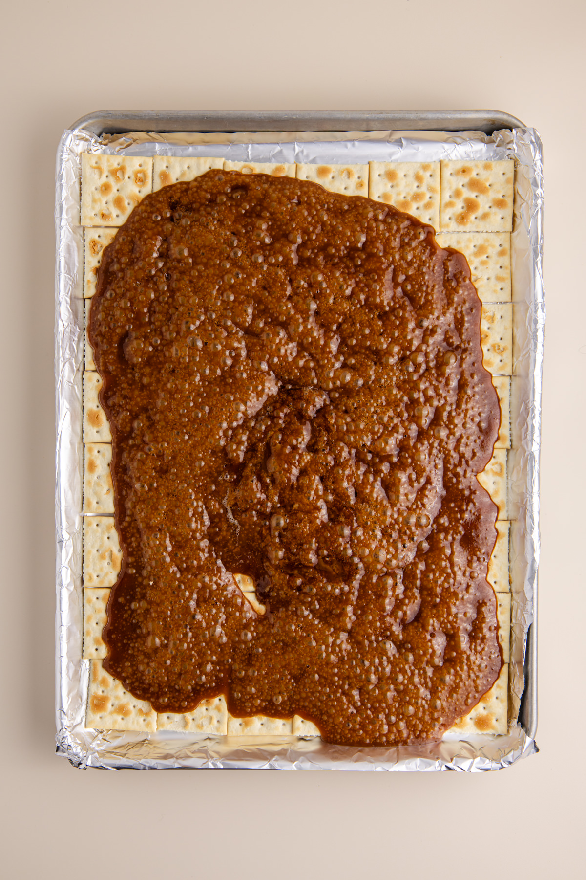 Caramel poured and spreading over crackers . on rimmed baking sheet