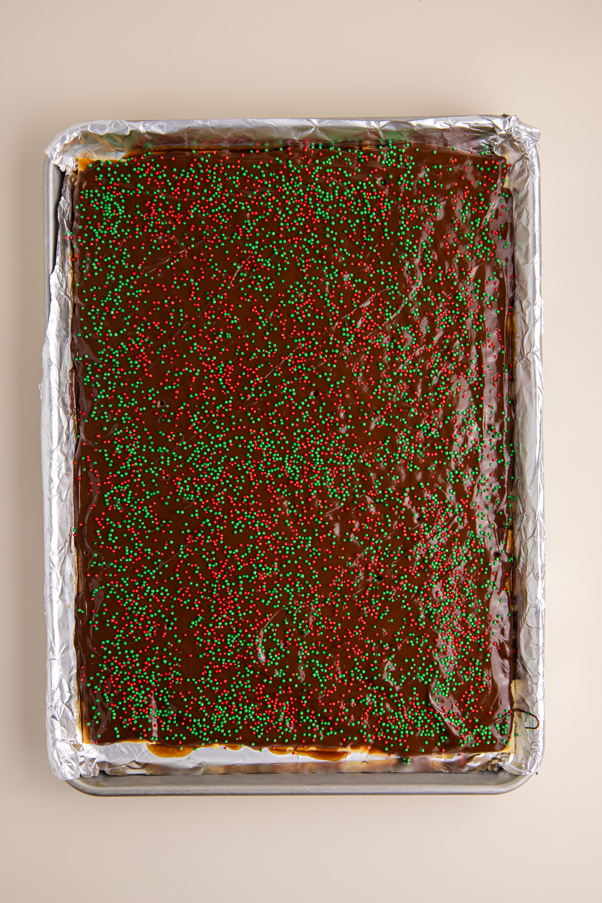 Caramel covered crackers with melted chocolate spread all over covered in sprinkles on rimmed baking sheet