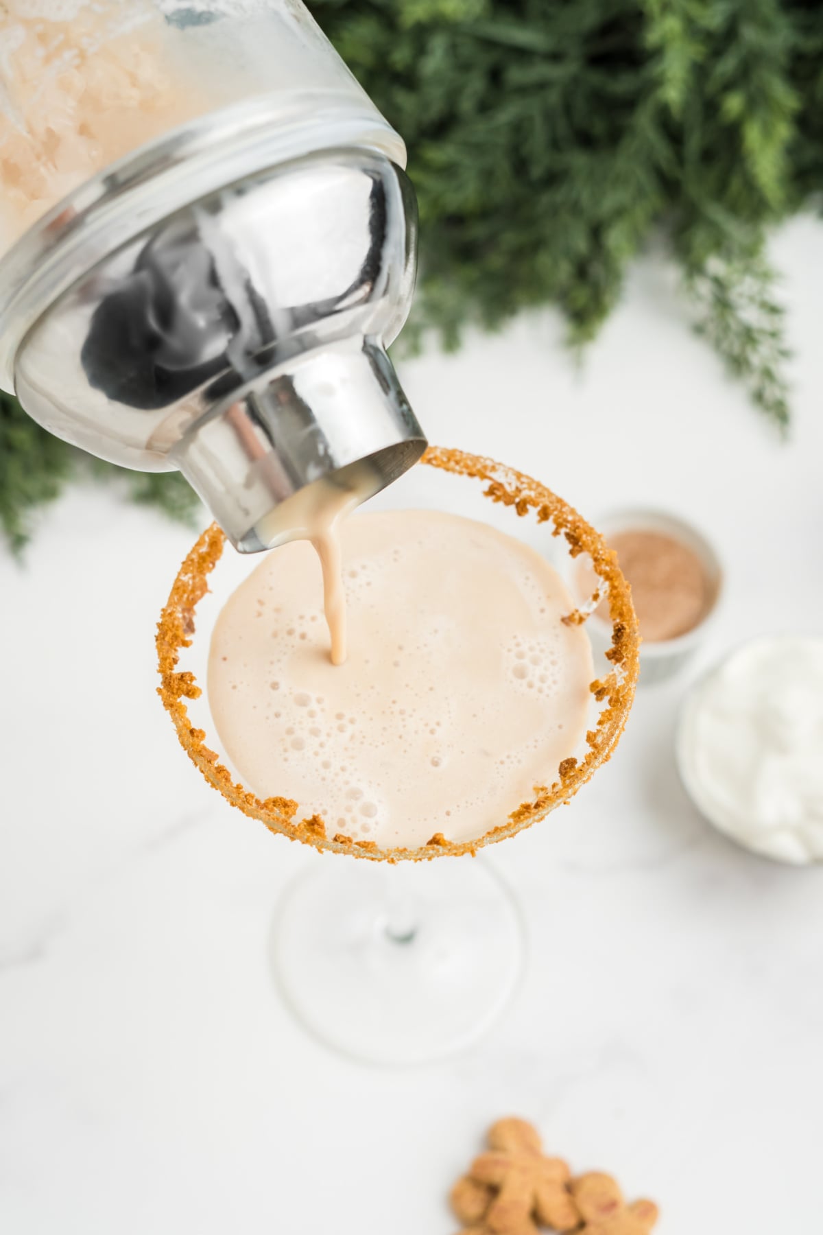 The cocktail being poured into the rimmed glass.