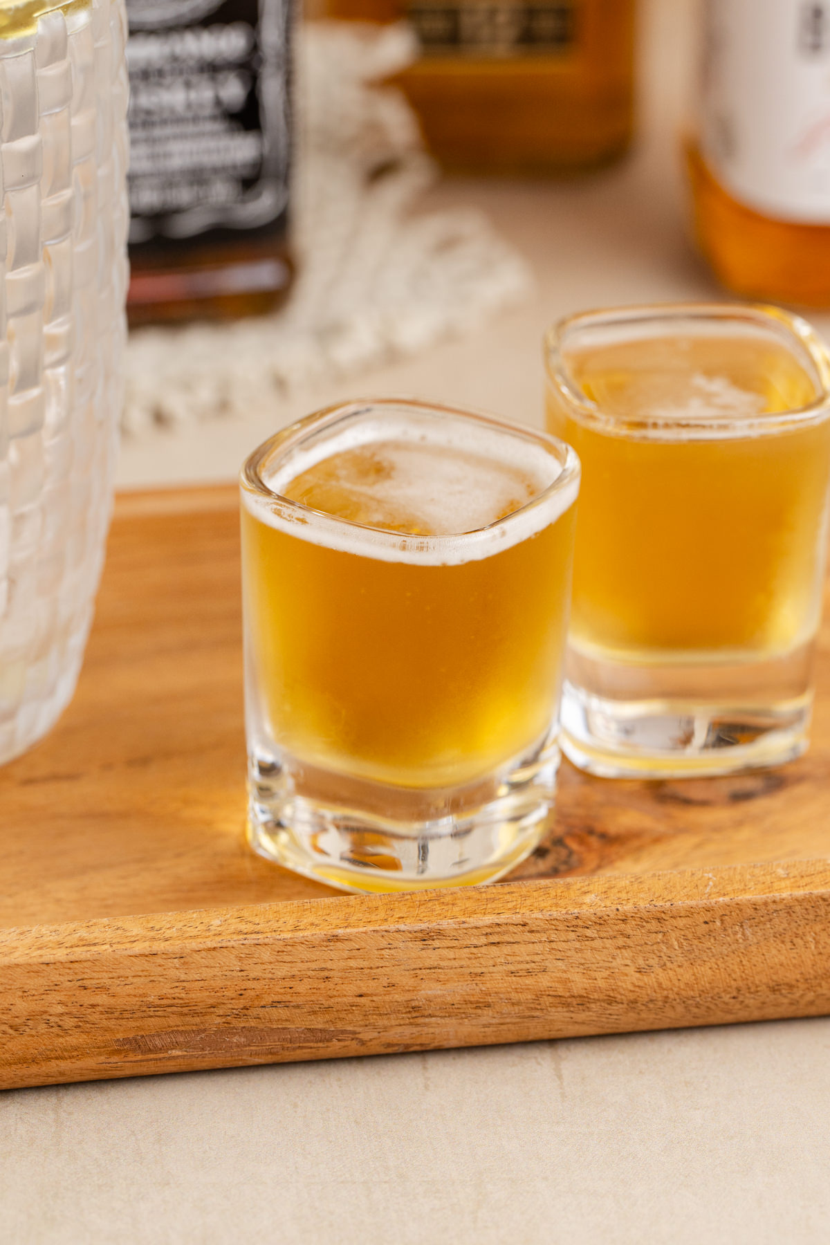 Two shot glasses filled with a whiskey shot on a board.