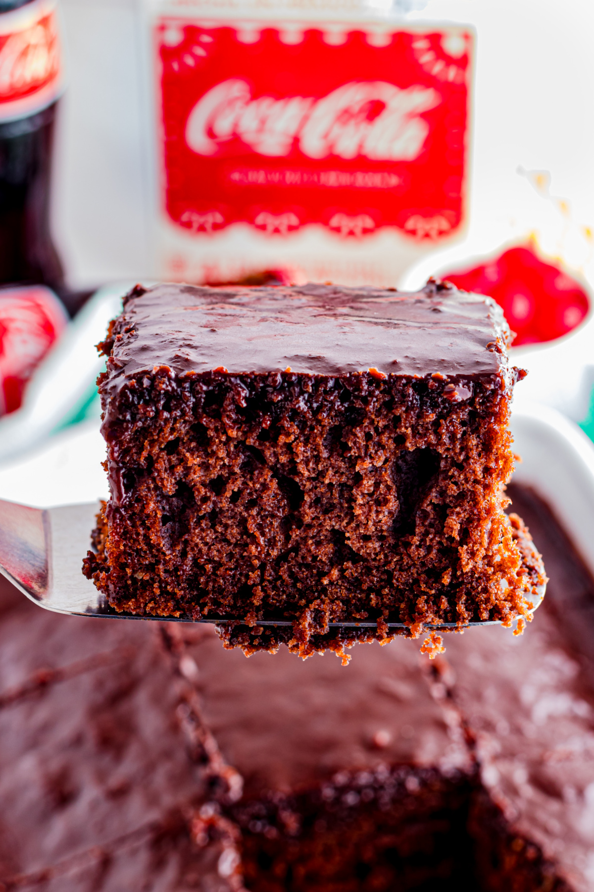 A slice of chocolate cake being held up in the air with a spatula.