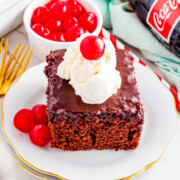 Piece of cake on a plate topped with whipped cream and a cherry