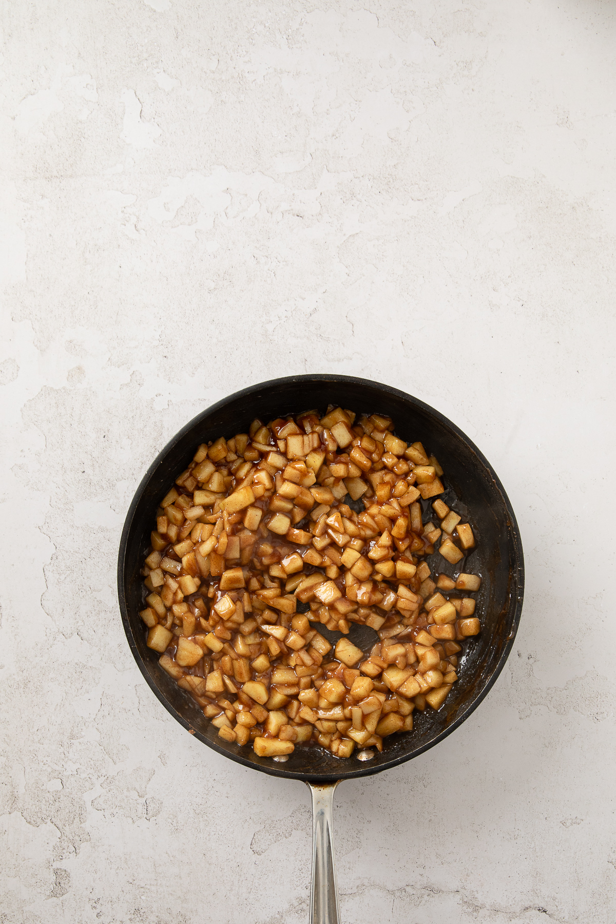 Diced apples with butter, sugar, spices, and lemon juice in a skillet.