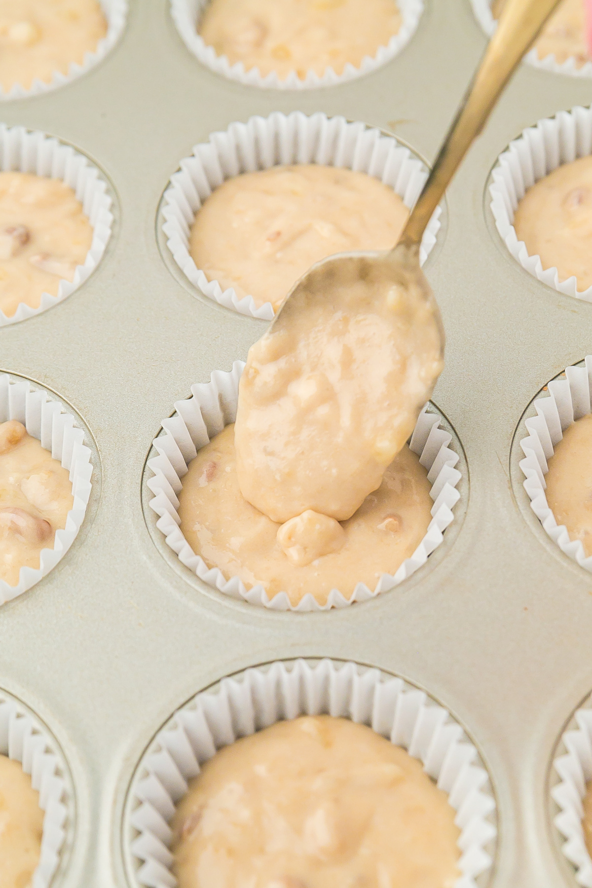 Muffin batter being added to muffin pan filled with liners using a spoon.
