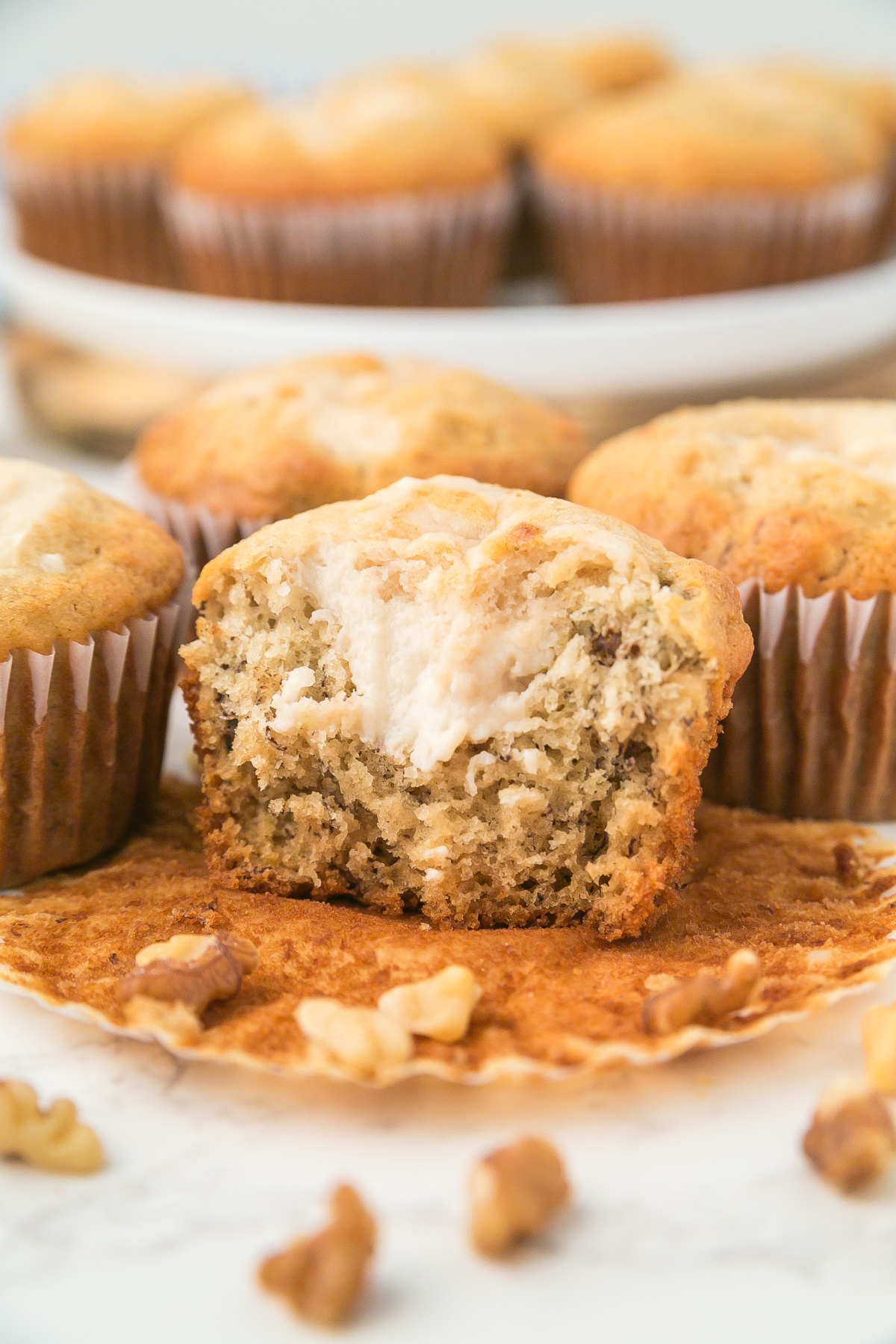  Banana cream cheese muffins on a counter with the muffin in front missing a bite showing the cream cheese in the center.