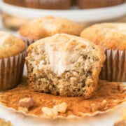 Banana cream cheese muffins on a counter with the one in front missing a bite and cream cheese is in the center.