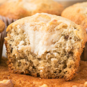 A pile of banana muffins with top one cut in half showing cream cheese.