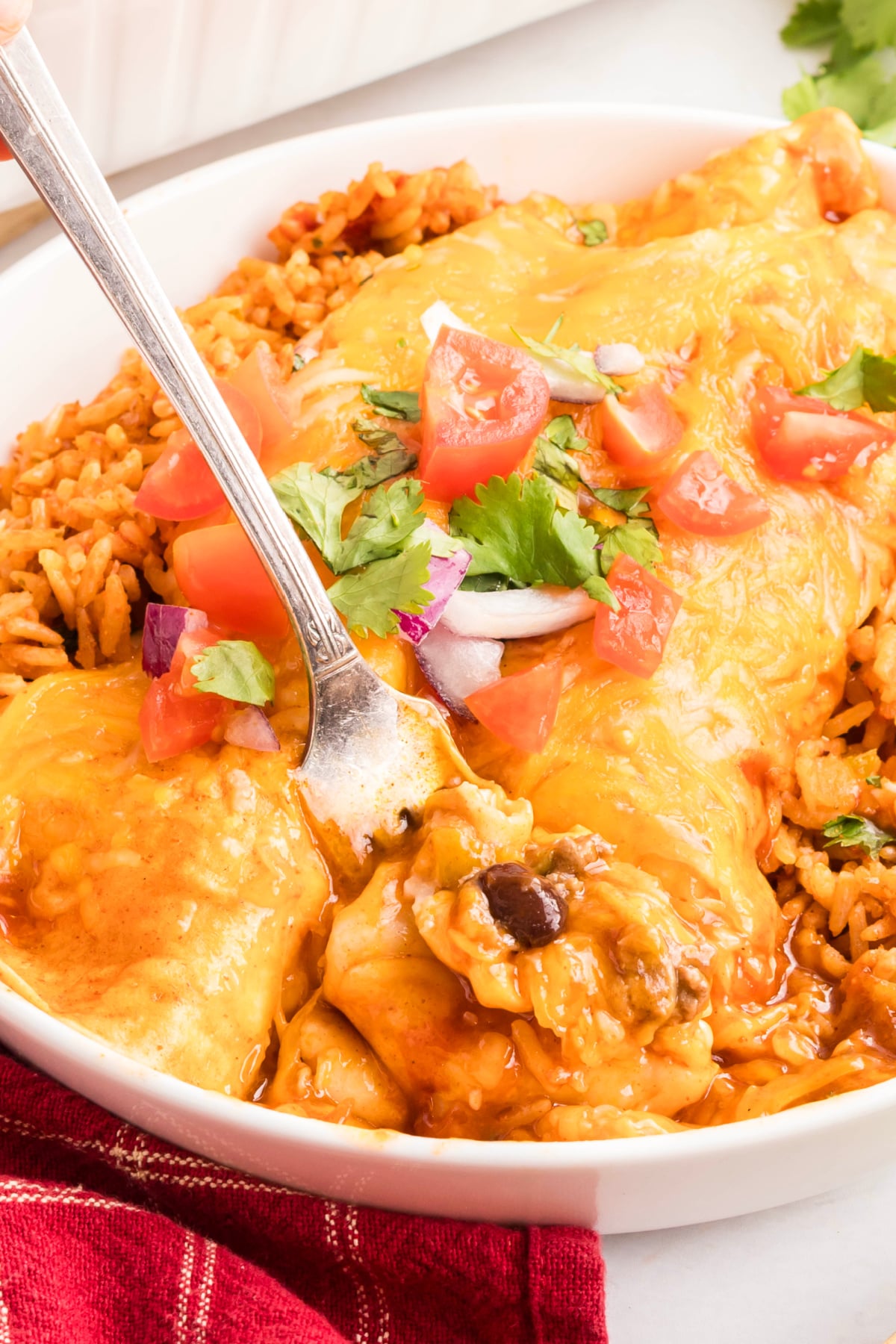A fork taking out a bite of beef enchiladas from the dish.