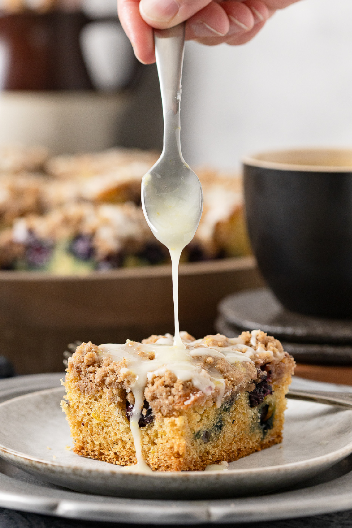 A slice of blueberry sour cream cake with glaze being poured over it.