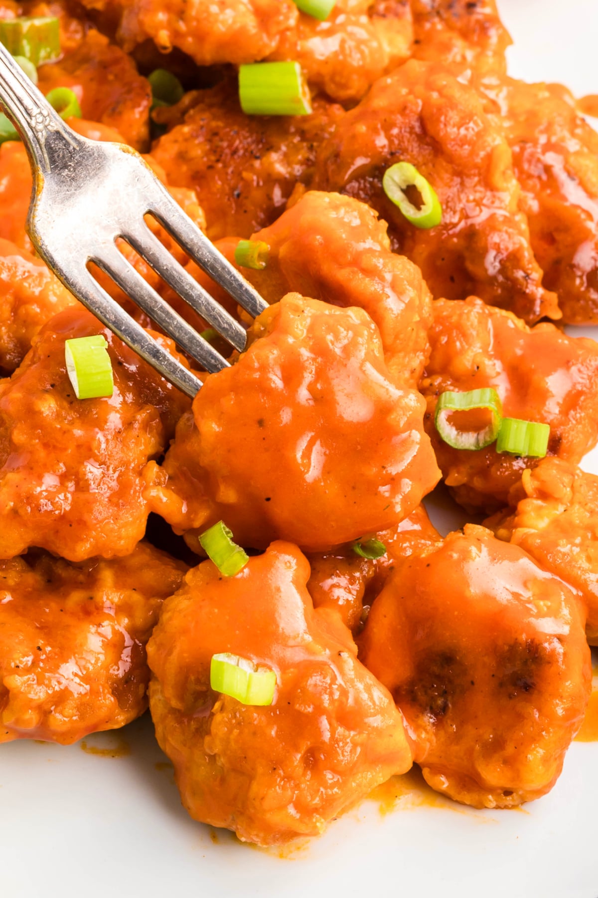 A fork taking a boneless buffalo chicken wing off the plate.