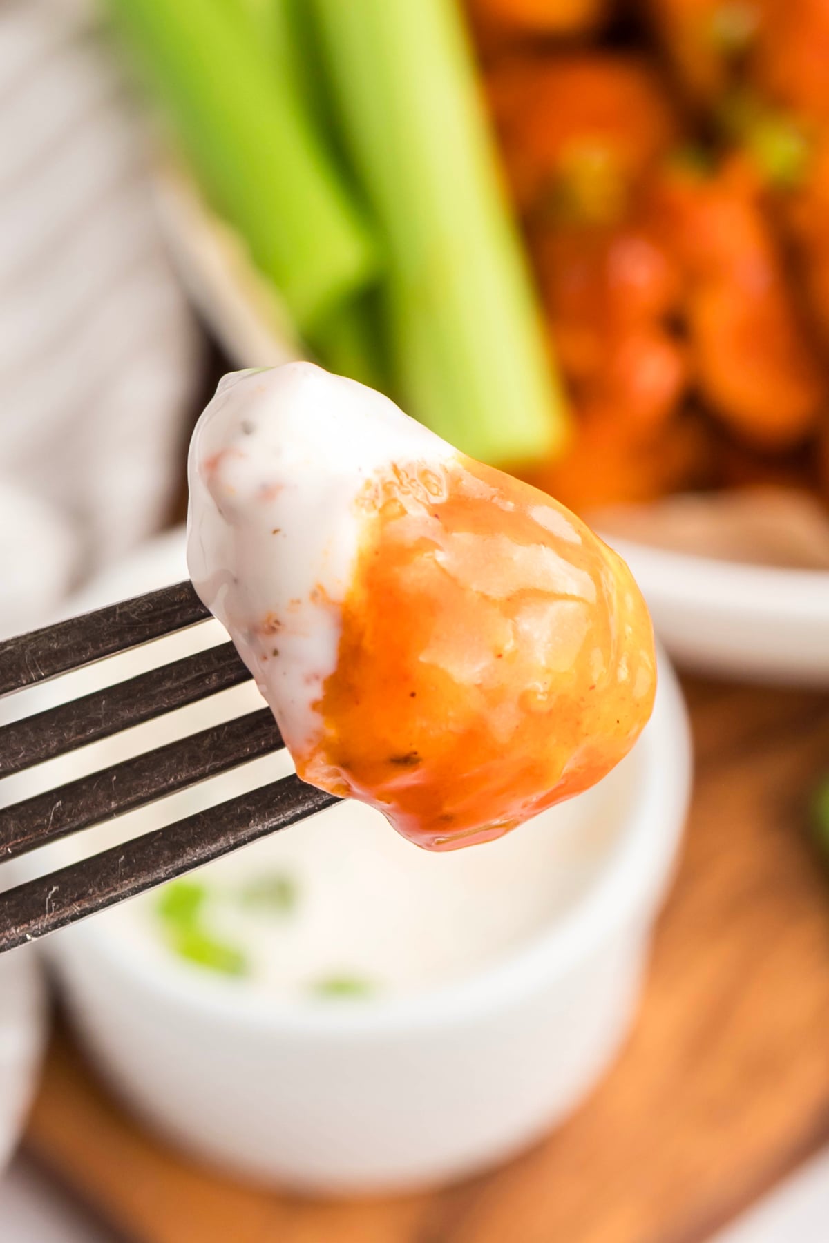 A piece of boneless chicken with buffalo sauce and dip held up in the air.