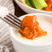 Boneless buffalo chicken wings being dipped into sauce.