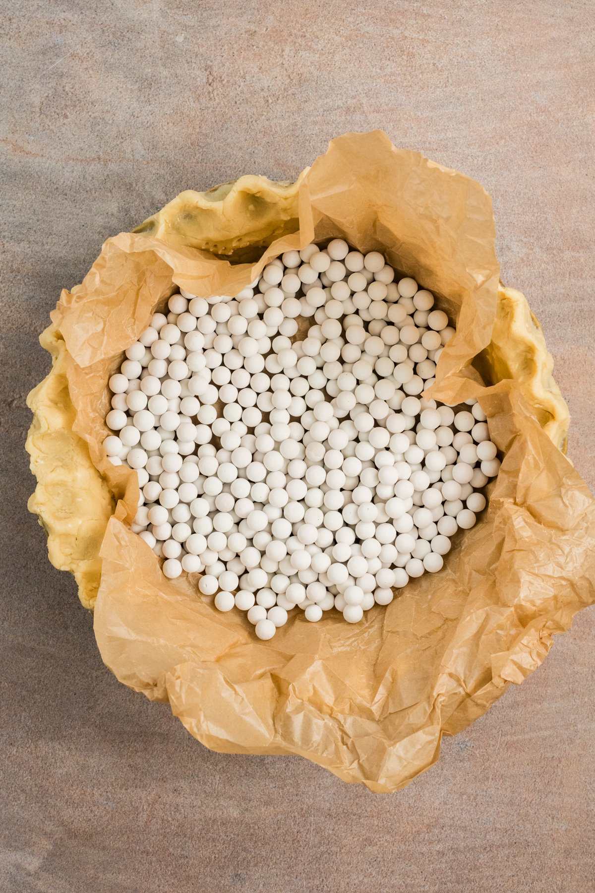 Pie crust weighed down by pie weights on parchment paper.
