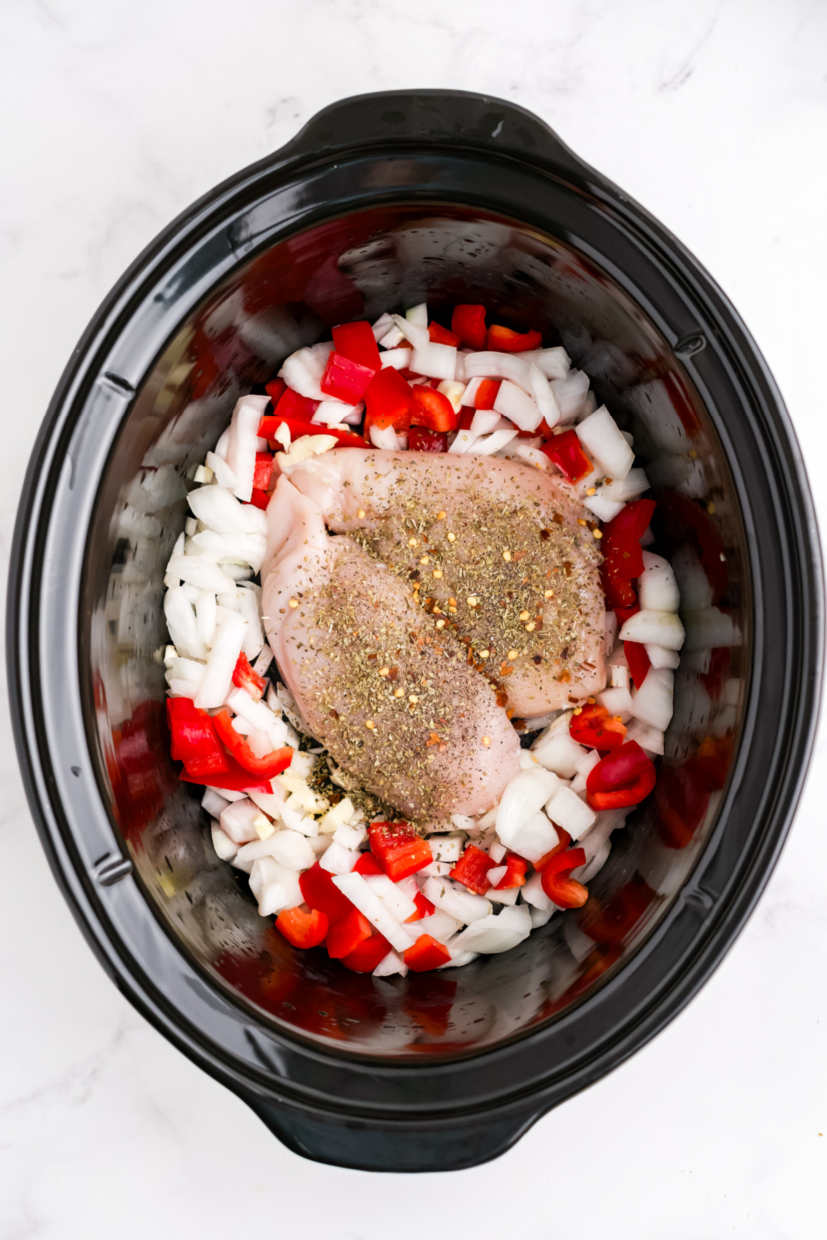 Chicken breasts on the bottom of the slow cooker with bell peppers, onions, and garlic.