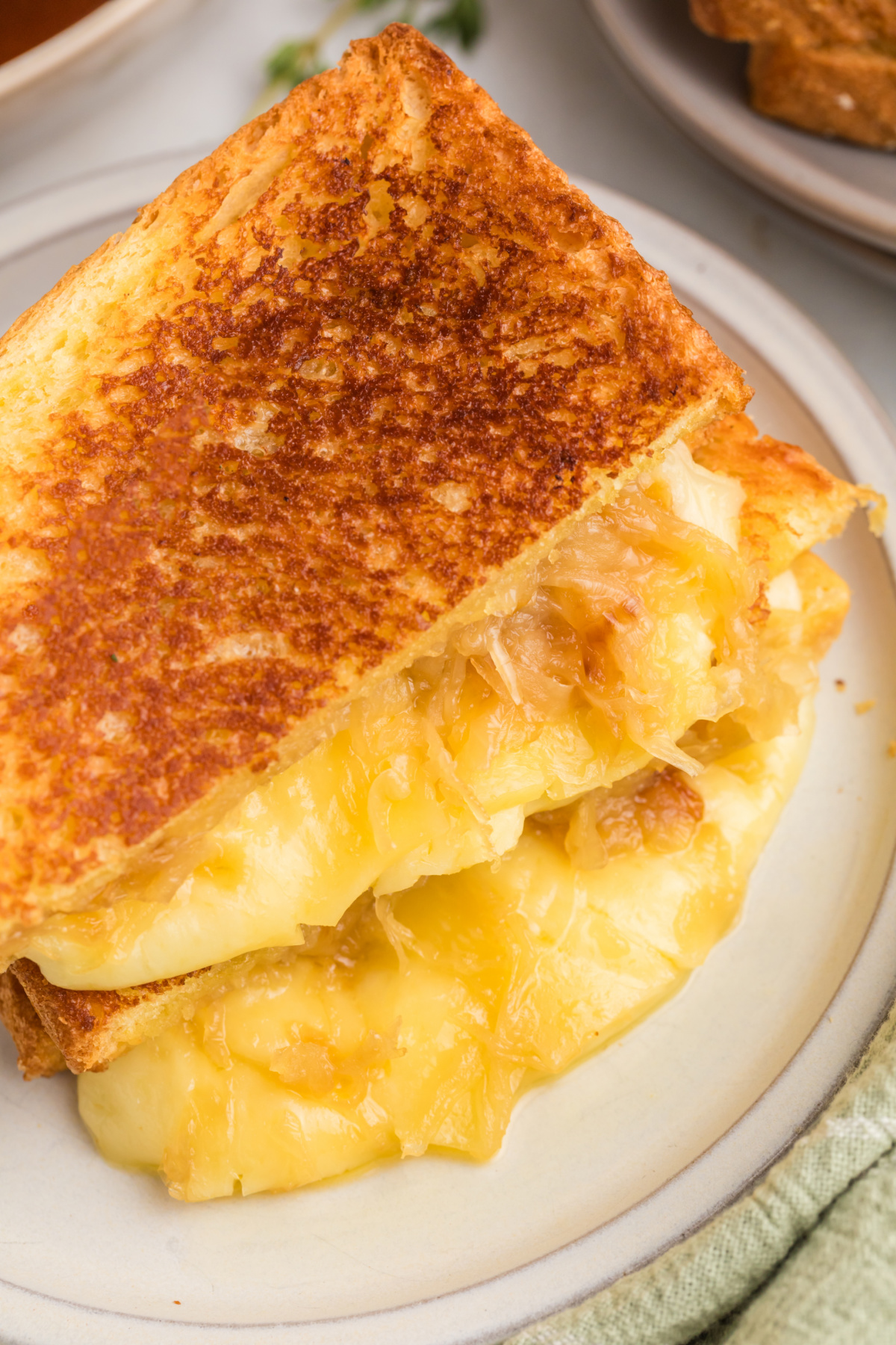 A sandwich with cheese and fried onions oozing out on a plate.