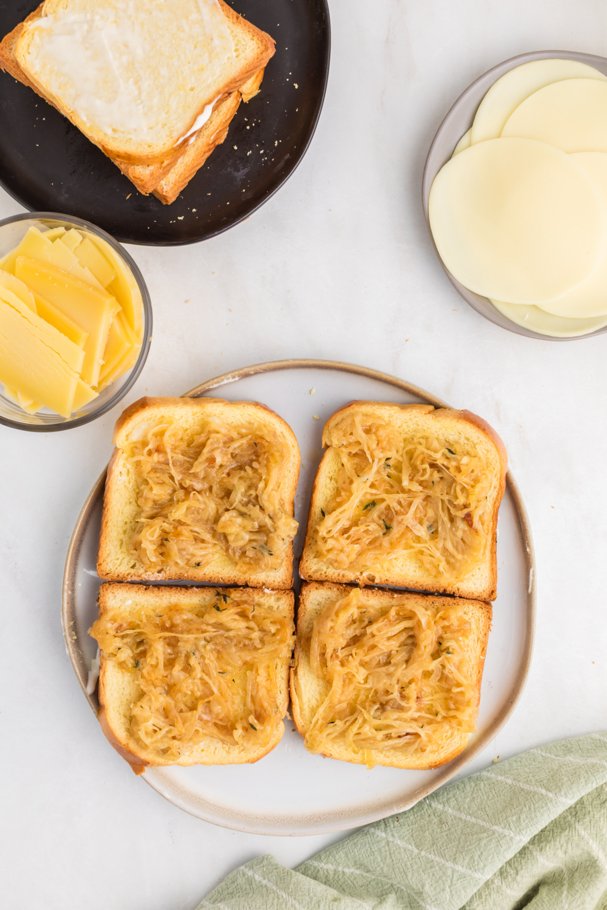 Four grilled cheese sandwiches being constructed with onions on top.