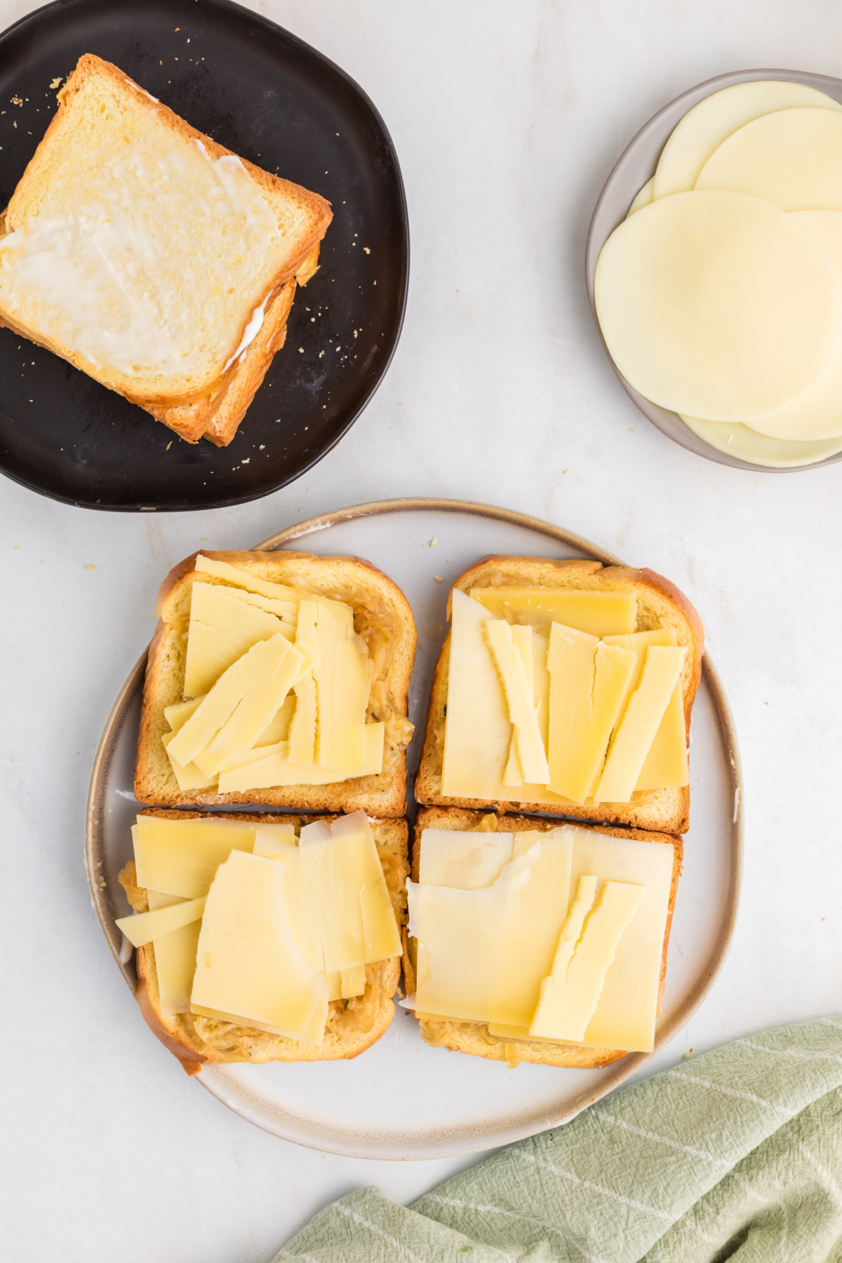 Four grilled cheese sandwiches being constructed gruyere on top of the onions.