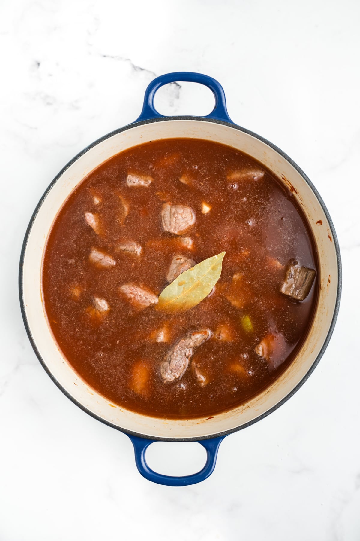 Tomato sauce, broth, sugar, beef, spices, and bay leaf added to the stew.