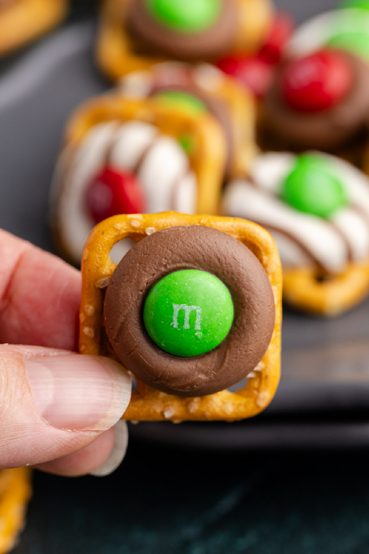 A pretzel, chocolate and M&M held up in the air.