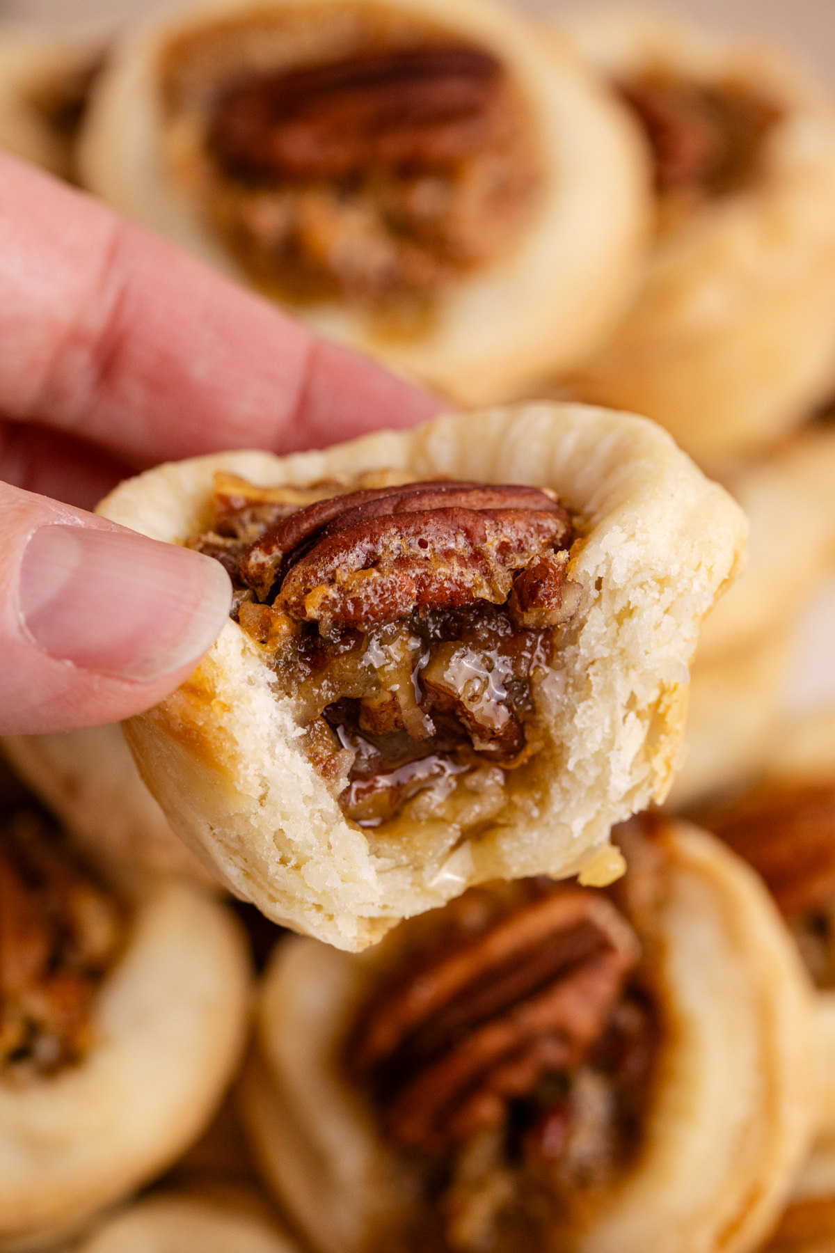 A tart with pecans being held up in the air with a bite taken out.