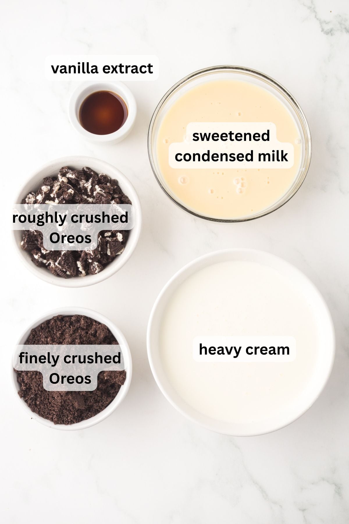 All of the ingredients needed to make Oreo ice cream in bowls on a table.