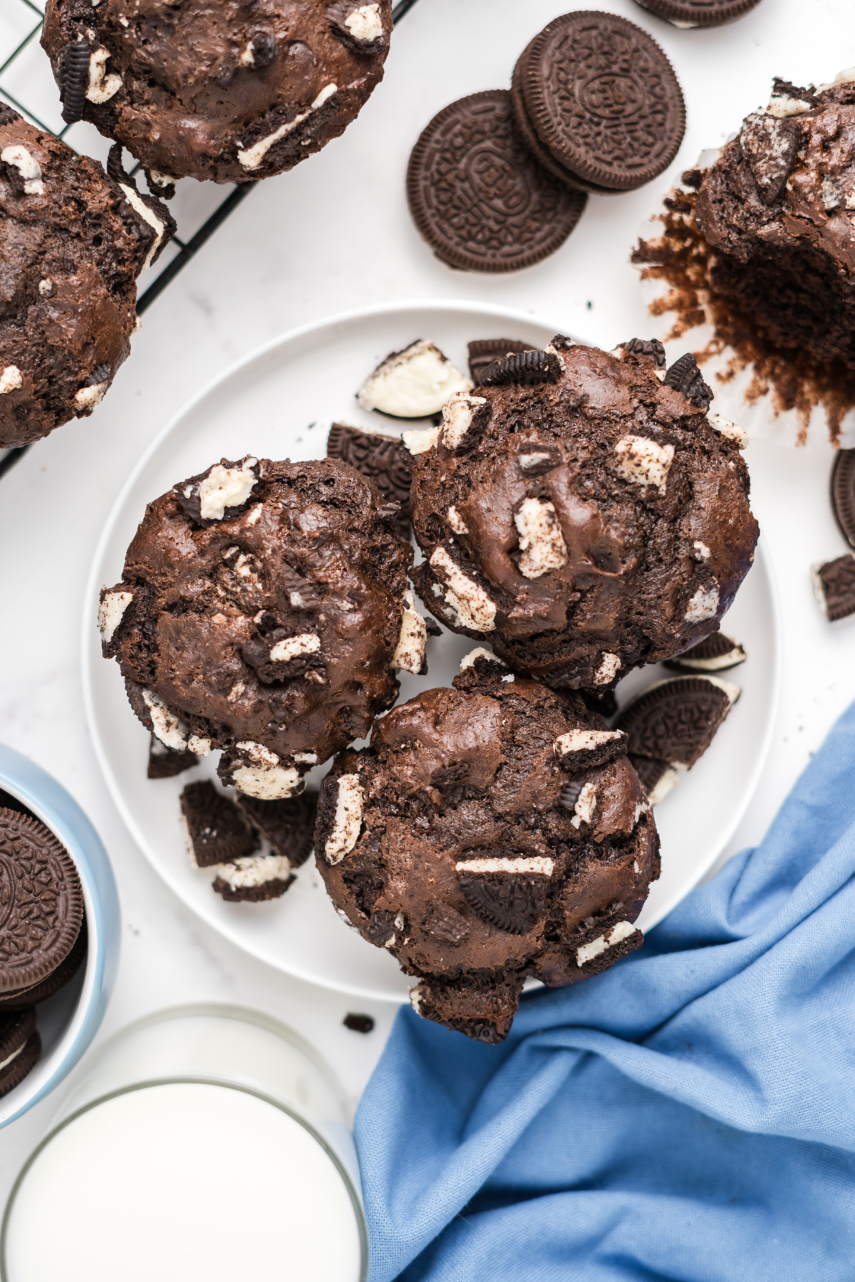 Three chocolate muffins on a plate with oreo cookies in it.