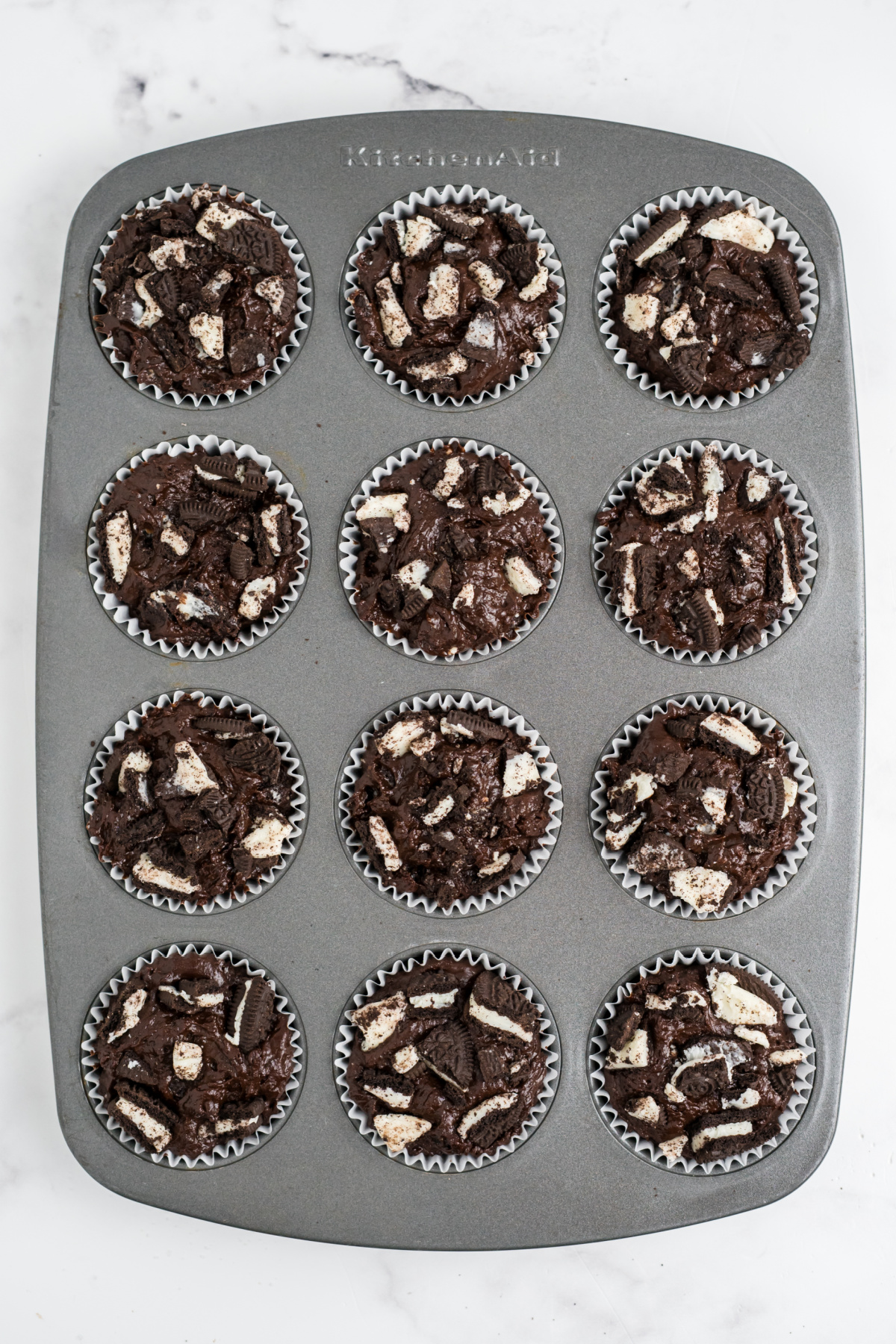 Muffin tin filled with batter and oreos on top.
