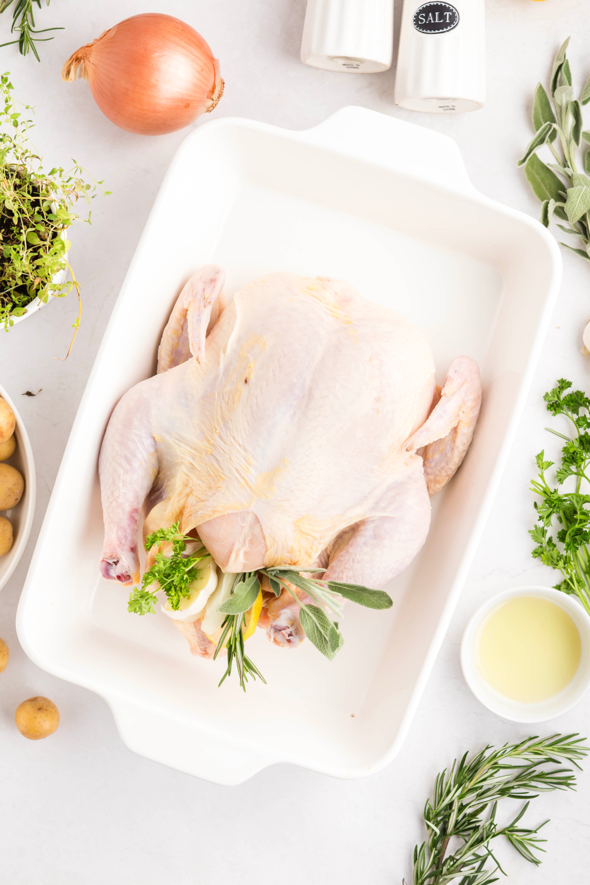 Uncooked whole chicken in baking dish with spices and herbs.