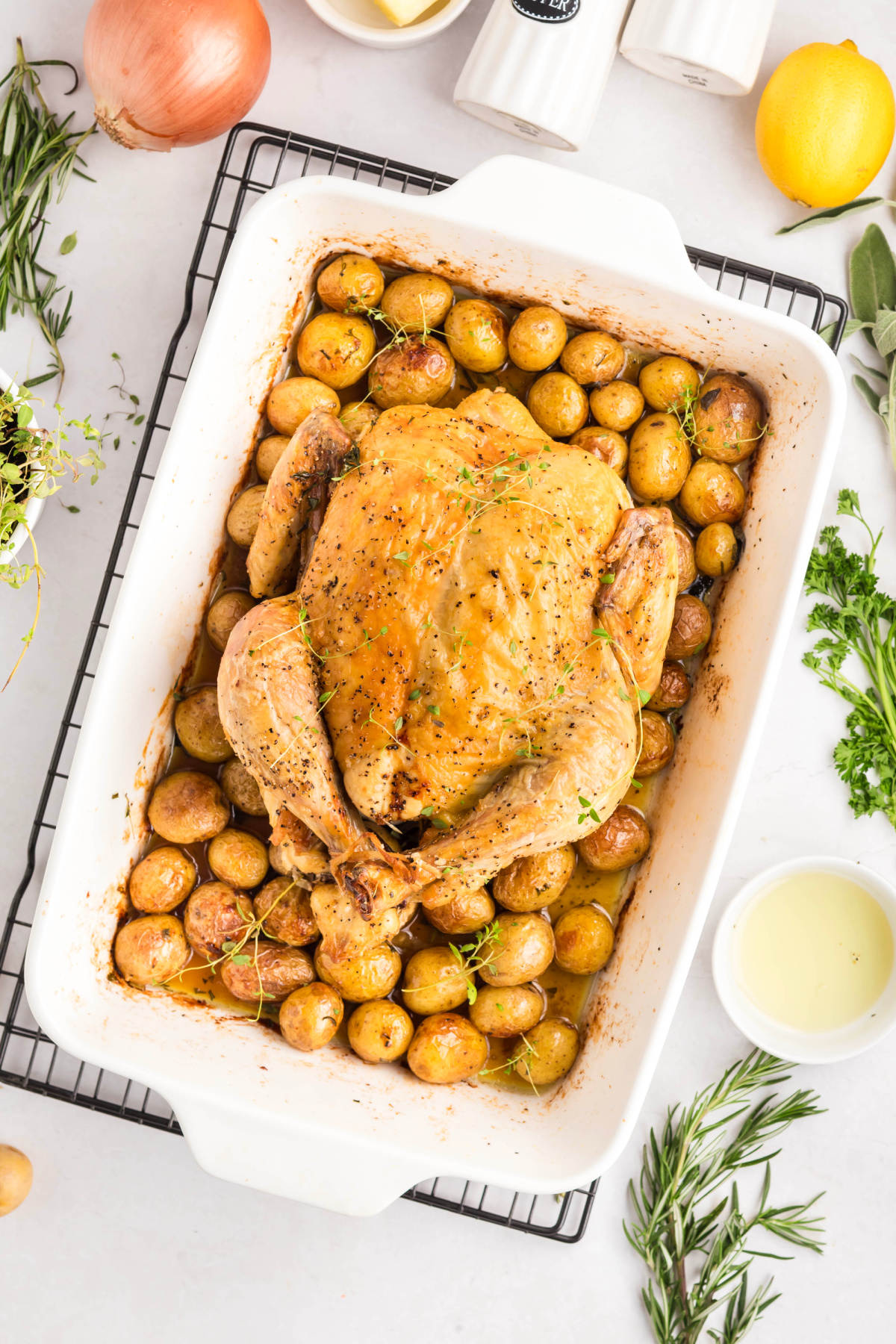 Roasted chicken in a pan on a bed of baby potatoes cooling.