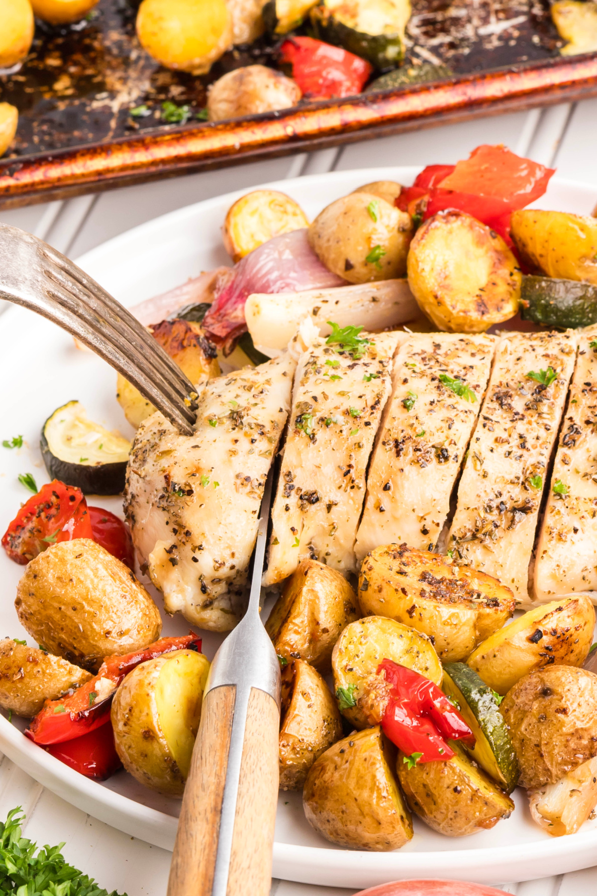 A fork and knife slicing up a piece of one pan chicken breast with vegetables. 