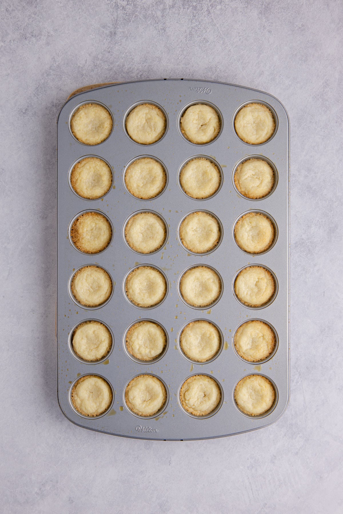 A spoon full of cookie dough put into each cavity of the muffin tray.