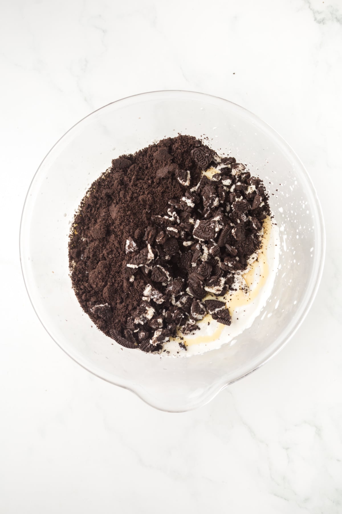 Whipped cream in a bowl with sweetened condensed milk and Oreo cookies being folded in.