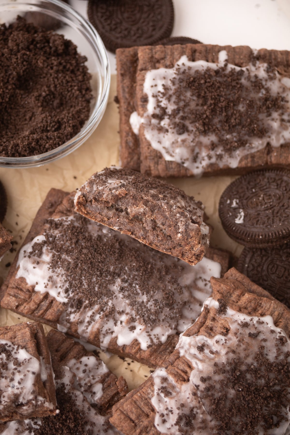 Oreo pop-tarts on parchment with Oreo cookies and one in the middle cut in half so filling is noticeable.