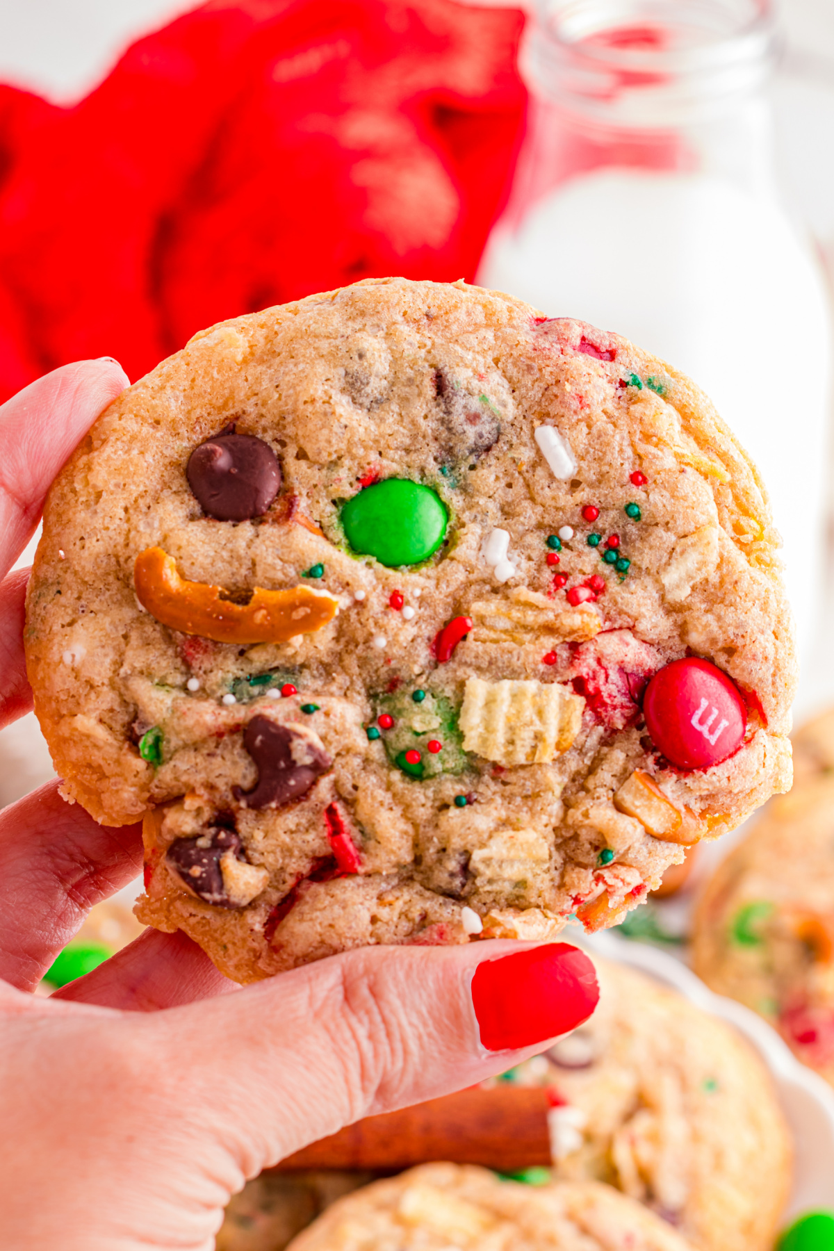 A cookie with pretzels, potato chips, M&Ms, and chocolate chips being held up in the air.