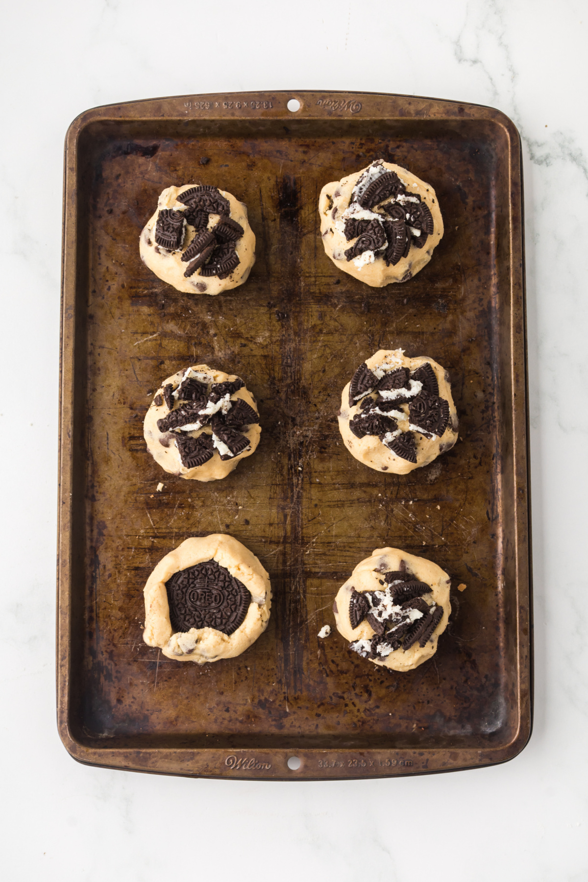 Stuffed Oreos on a baking sheet with chopped Oreos pressed on top.