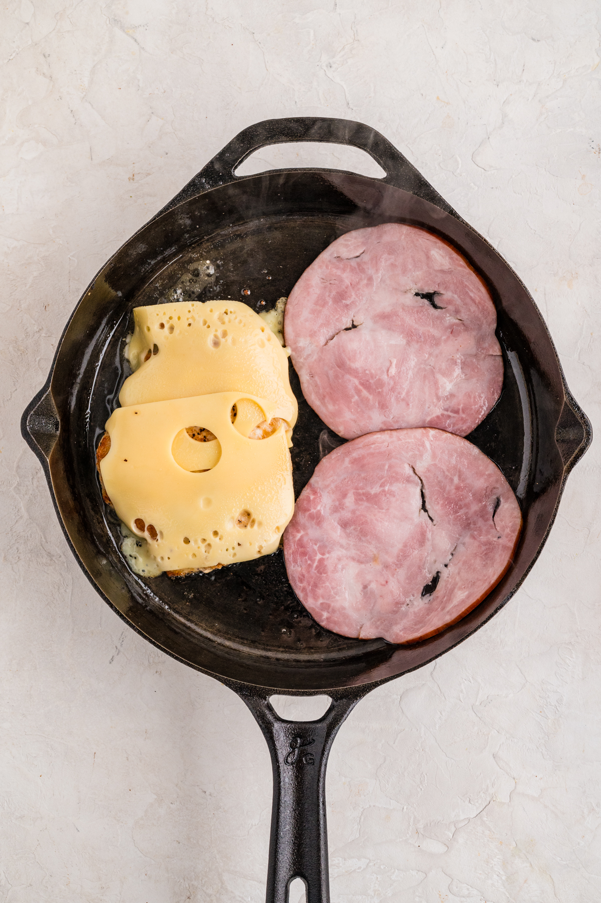 Cheese melting on the chicken and ham cooking in the skillet.