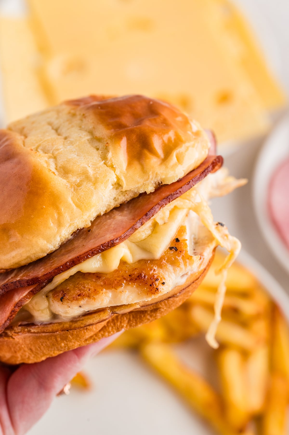 A sandwich with chicken, ham, and cheese being held up in the air.