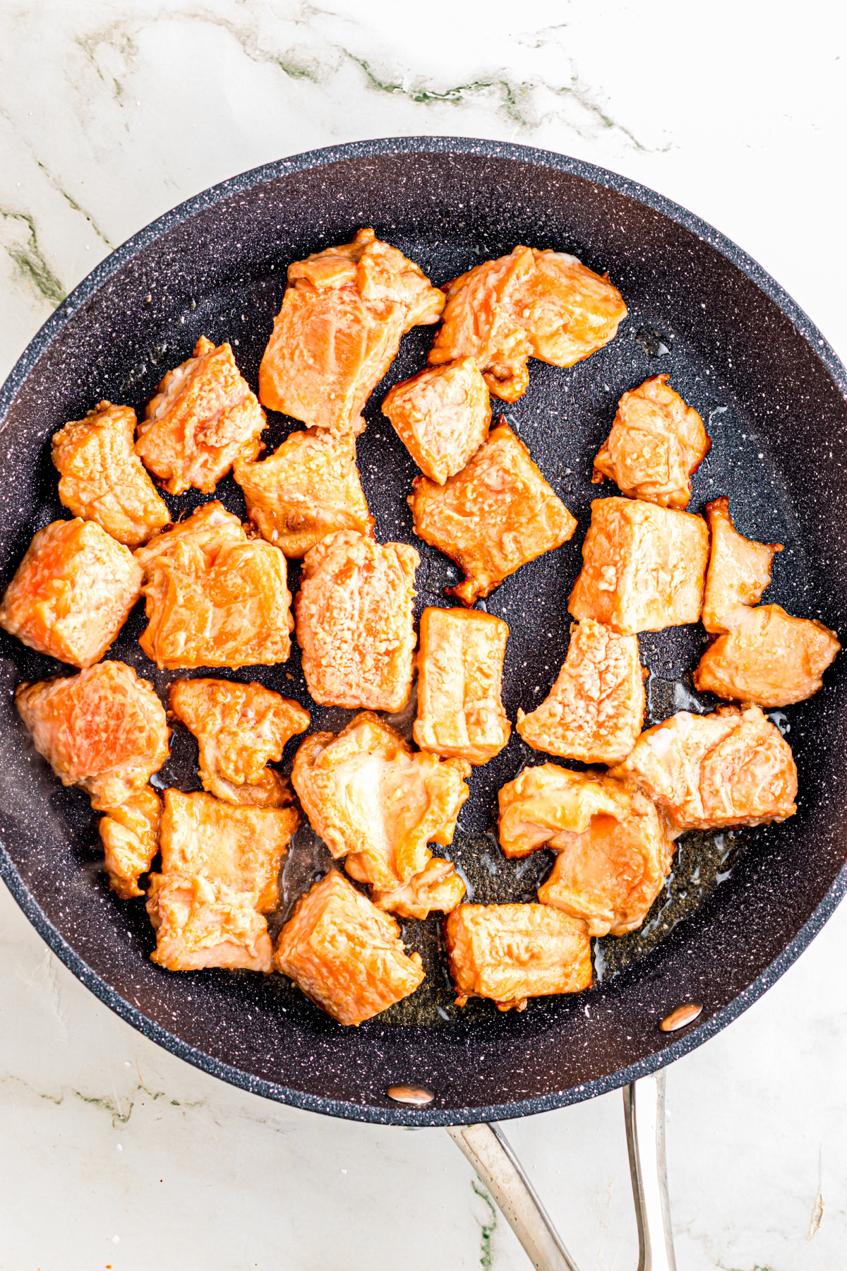 Salmon pieces searing on a skillet.