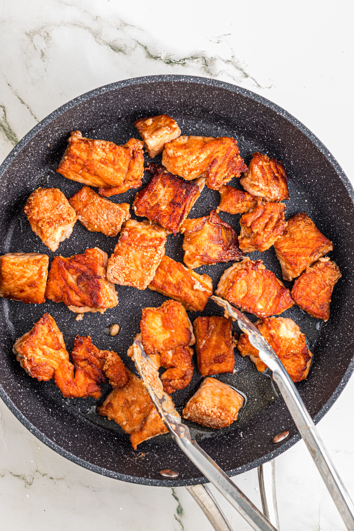 Salmon pieces cooking on a skillet.