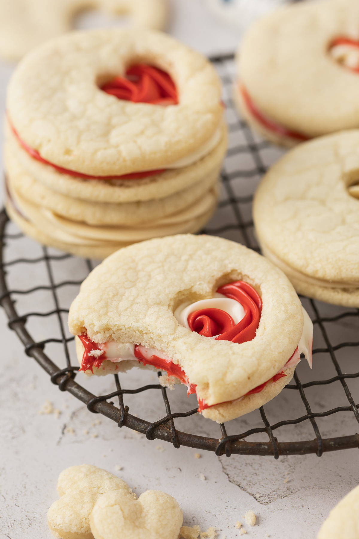 A sugar cookie with red and white frosting on a cooling rack and it is bitten into.