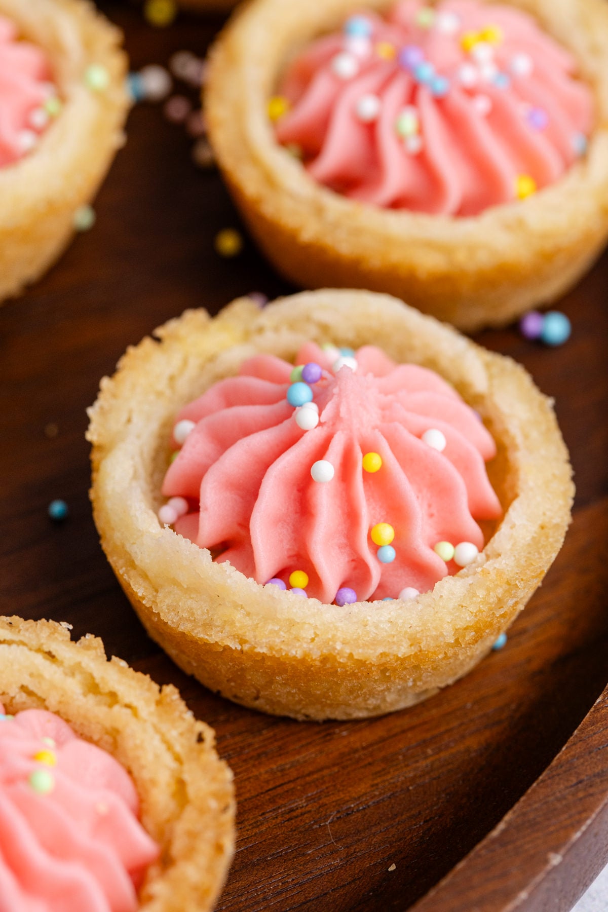 A cookie cup with pink filling and sprinkles on a table.