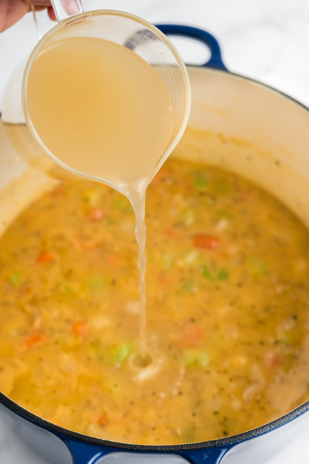 Chicken broth being poured into the dutch oven.