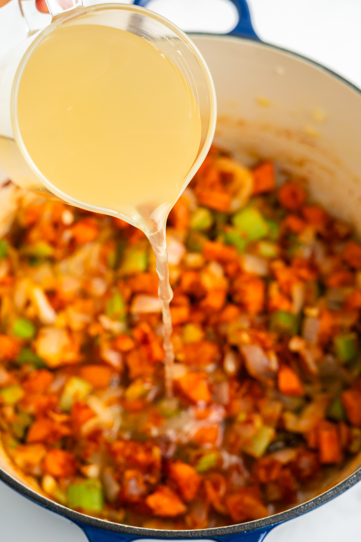 Broth pouring into the pot of vegetables.