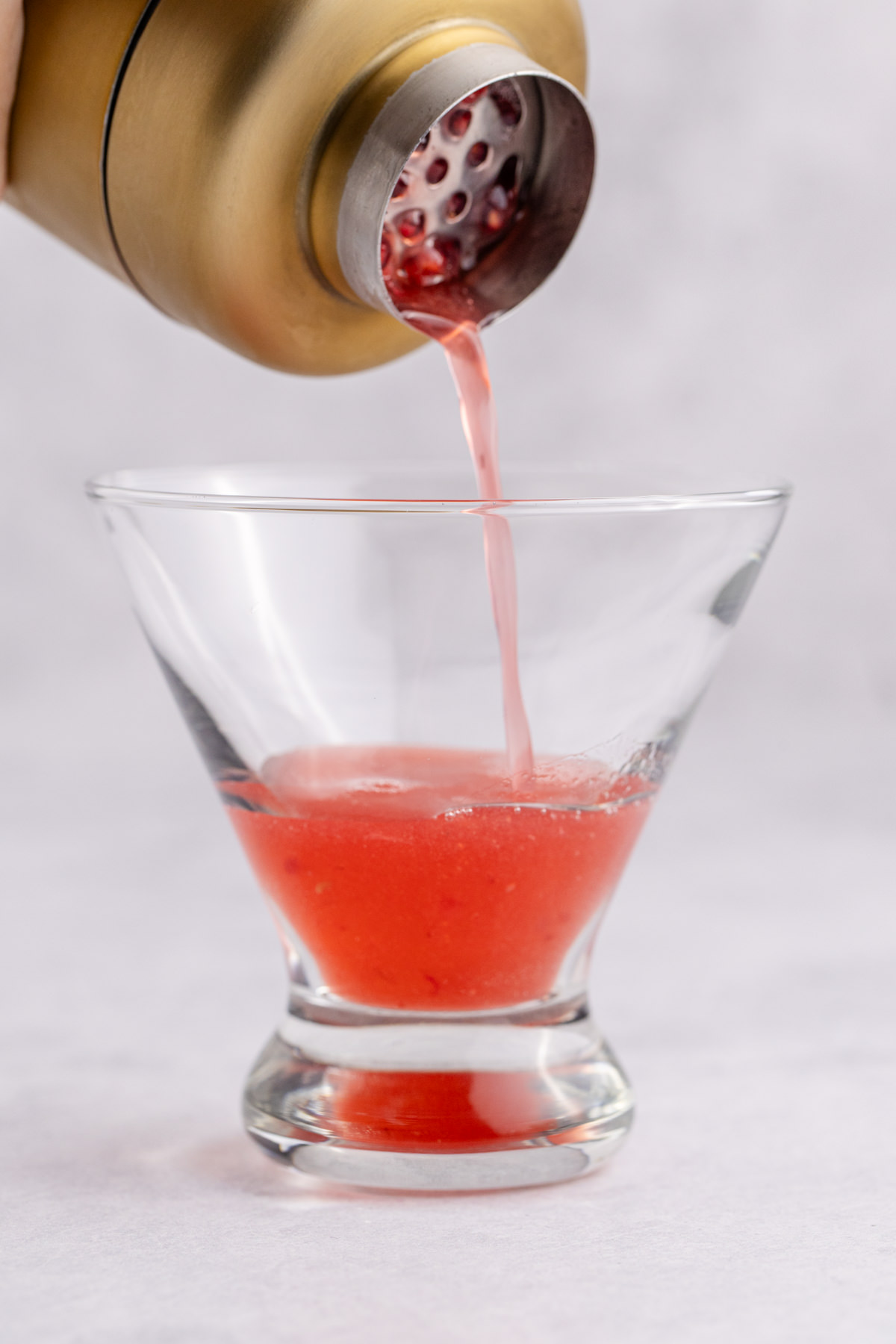 The shaken cocktail being poured into a glass.