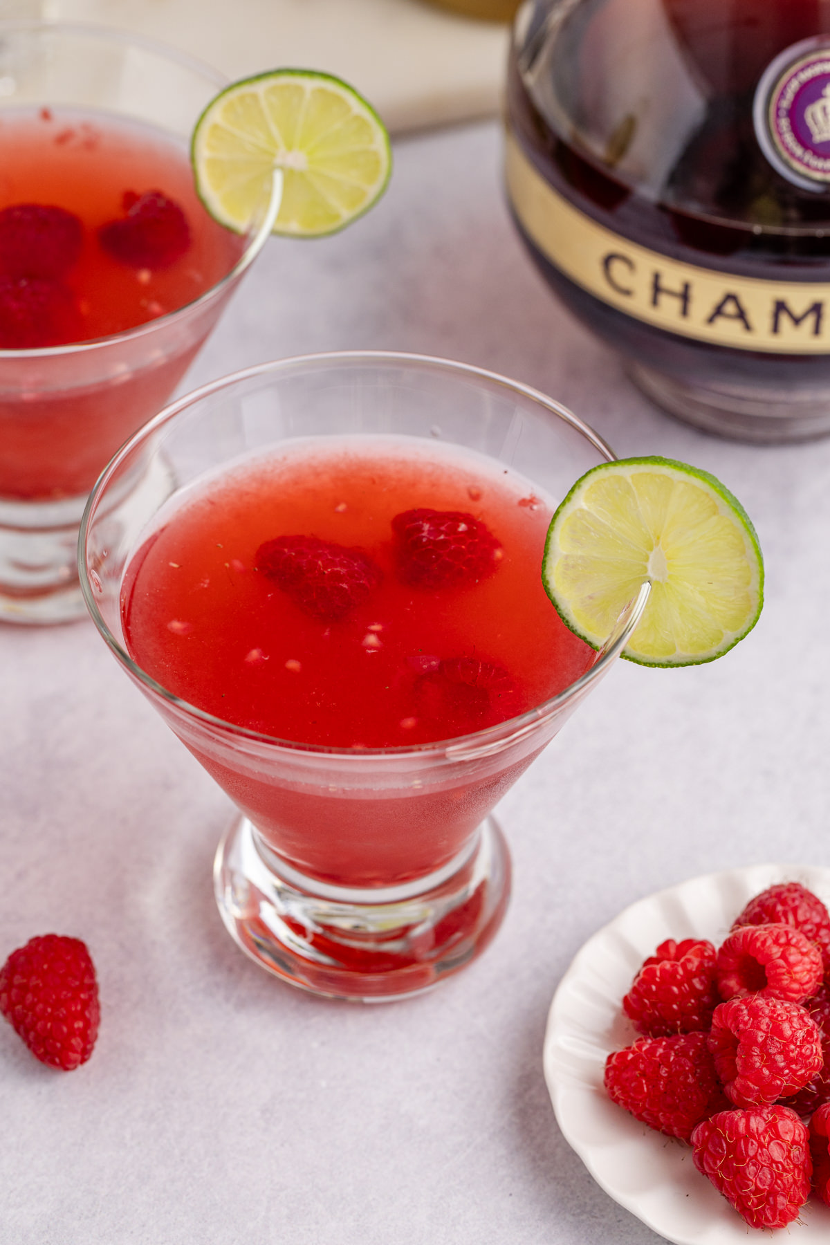 A martini in a glass with raspberries and a lime garnish.