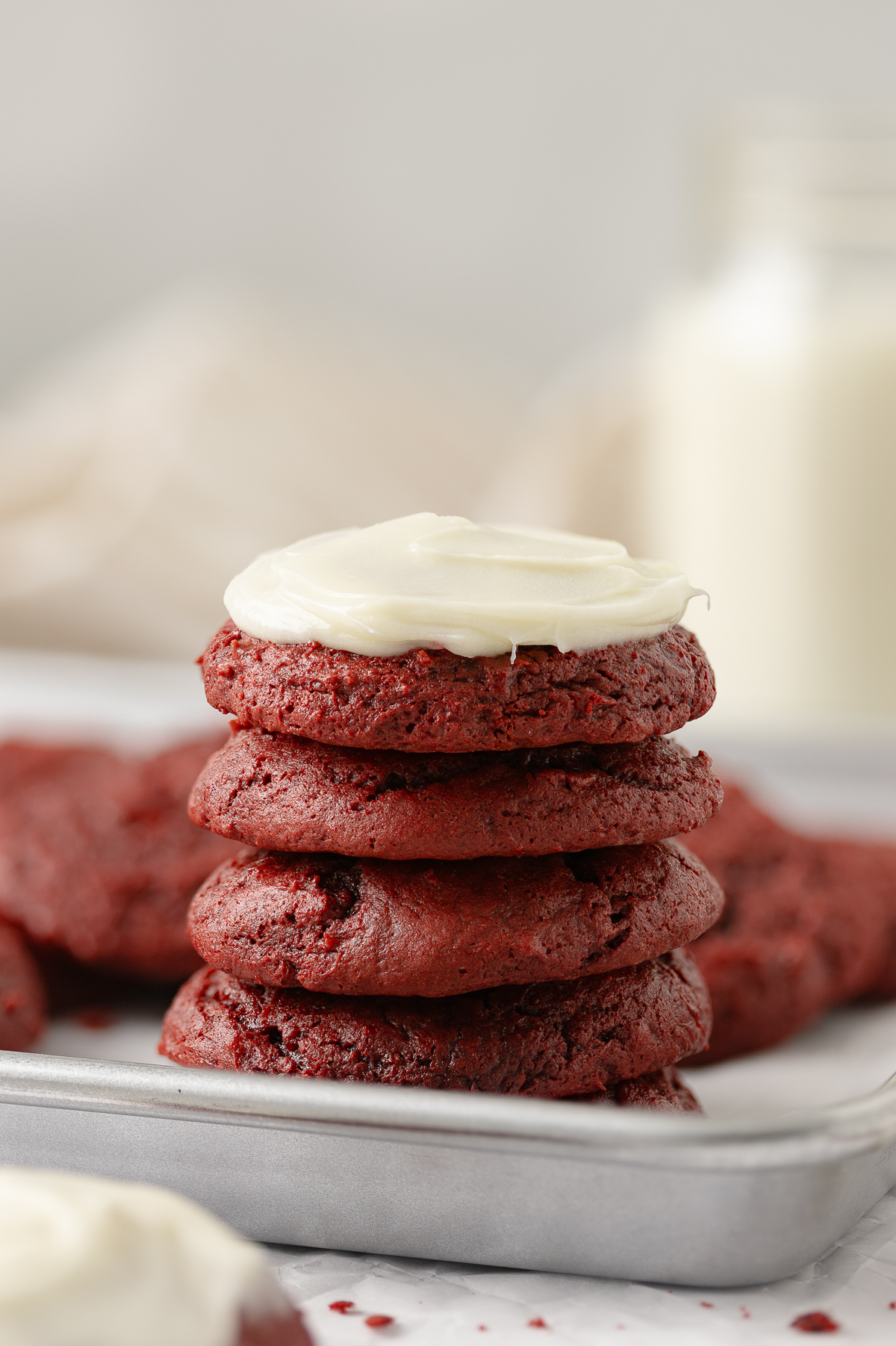 A stack of red velvet cookie with frosting on the top cookie.